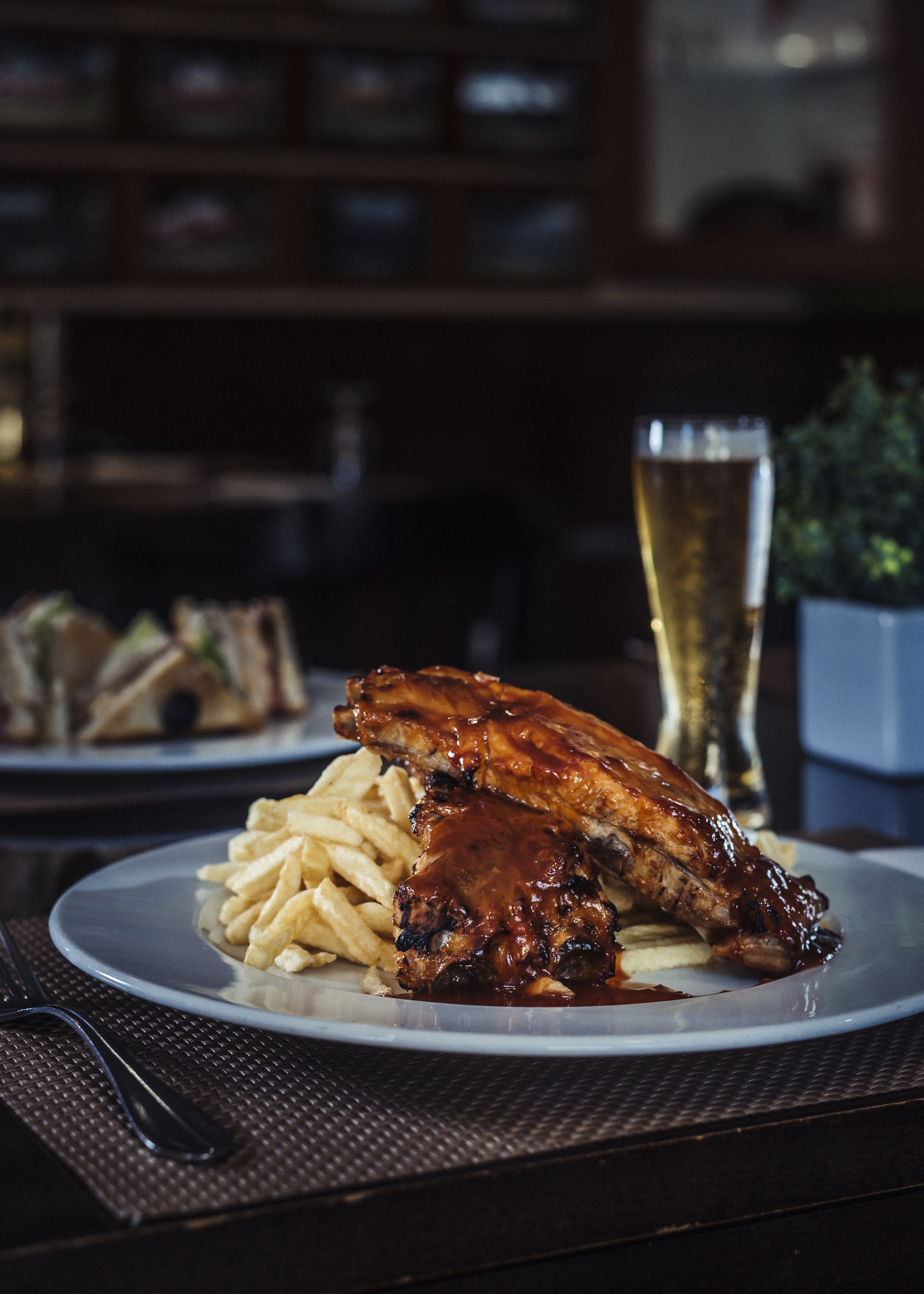 A plate of ribs with barbecue sauce and fries on a table.