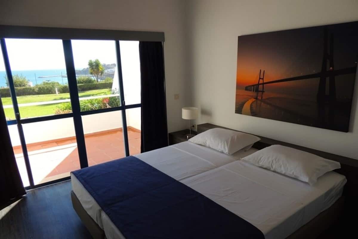 Une chambre d’hôtel avec un grand lit, une vue sur la mer par une porte coulissante et un tableau au mur.
