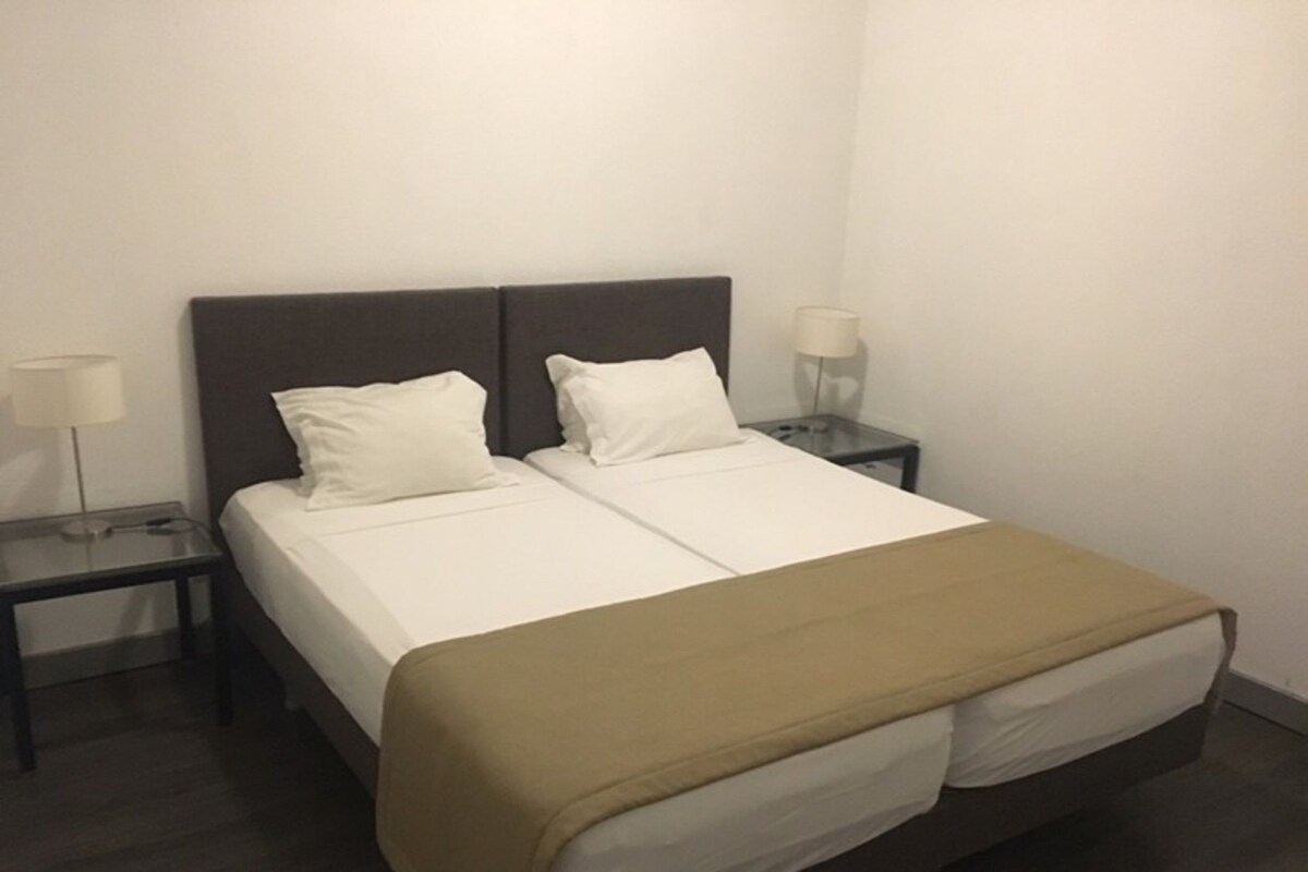 A hotel room with a double bed, two bedside tables, and two lamps.