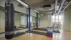 Een sportschool met houten vloeren, fitnessmatten, een bokszak en een spiegelwand.