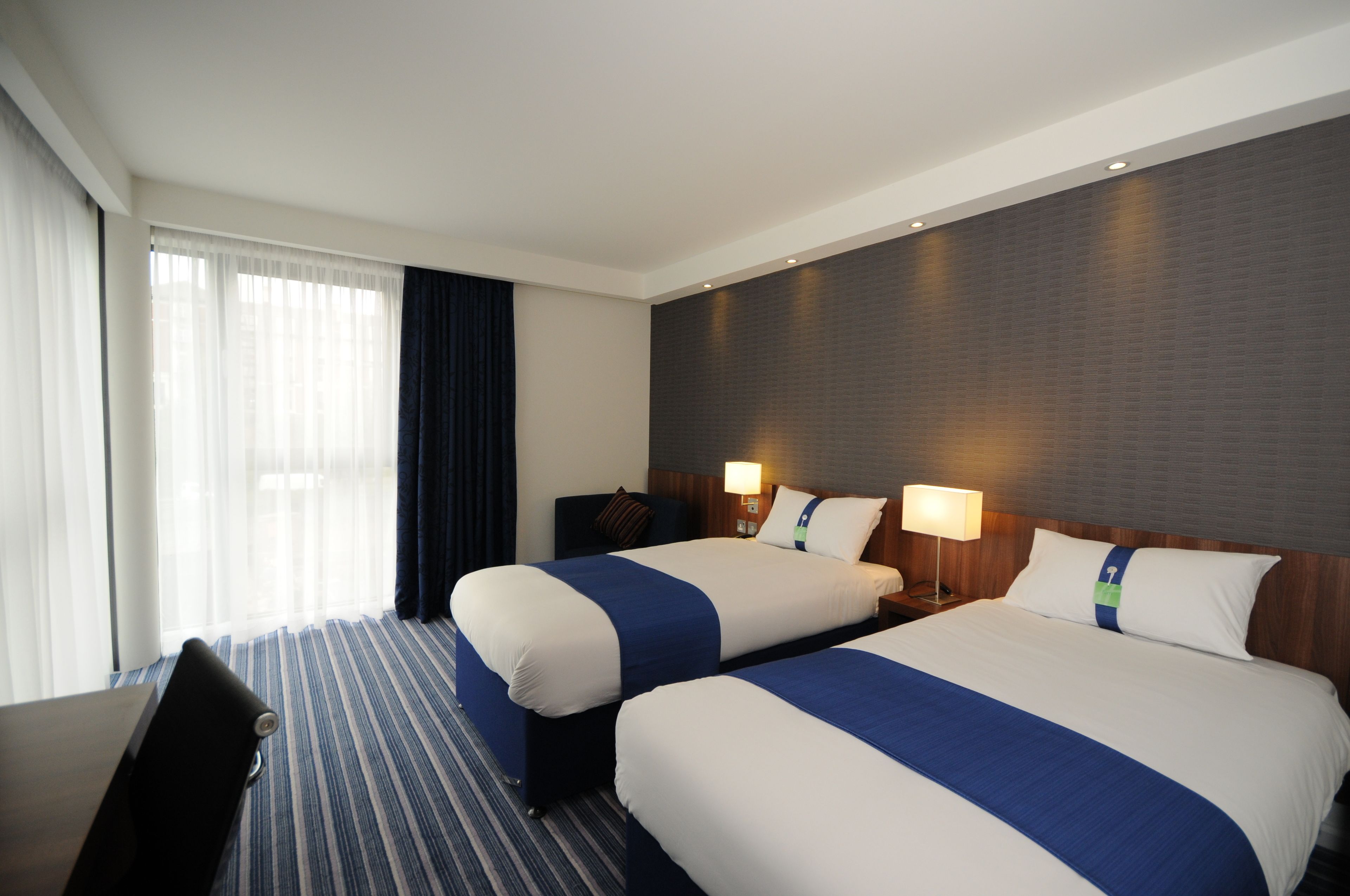 A hotel room with two beds, a desk, and a chair.