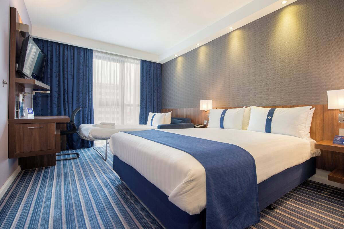 A hotel room with a large bed, a desk with a television, and a chair.