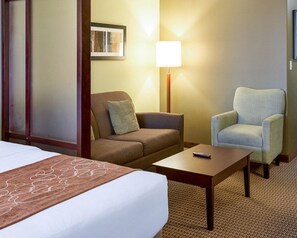 Quarto de hotel com cama, duas poltronas, uma mesinha, abajur e um quadro na parede.