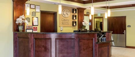 A reception area with a wooden reception desk, framed certificates, and a sign for 'Comfort Suites'.