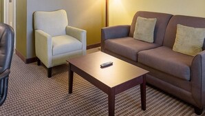 A hotel room with a beige armchair, a brown sofa, a wooden coffee table, and a floor lamp.