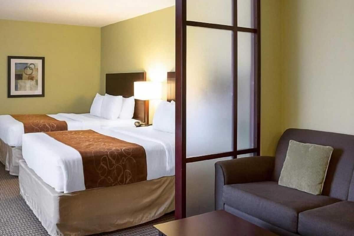 Een hotelkamer met twee bedden, een bank, een lamp en een groot raam.