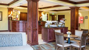 A hotel lobby with a reception desk, a seating area with a sofa and chairs, and a buffet counter with various food items.