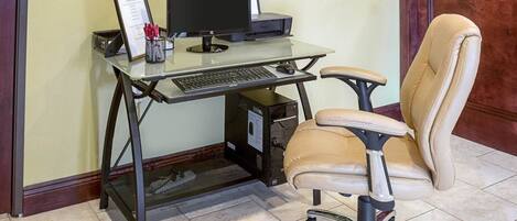 A home office setup with a glass desk, a computer, and a leather chair.