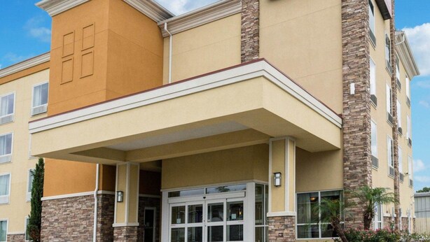 A Comfort Suites hotel with a beige and brown facade, a stone accent wall, and a clear blue sky.