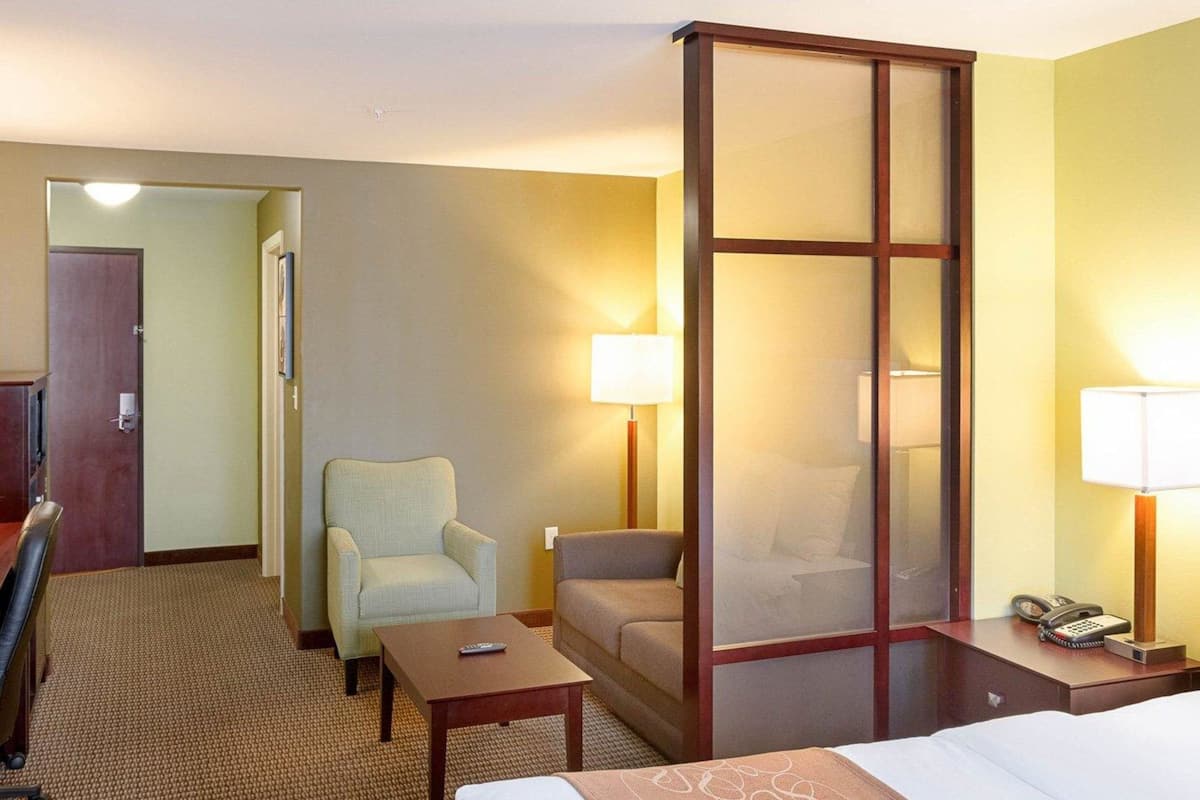 Een hotelkamer met een bed, een stoel, een klein tafeltje, een nachtkastje met een lamp en een groot raam met uitzicht.