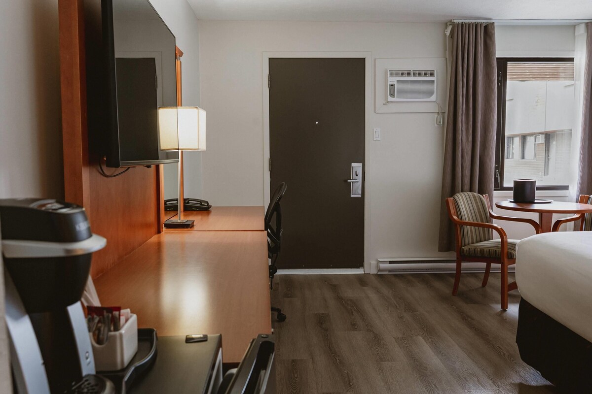 A hotel room with a bed, a desk with a lamp, a chair, a television, and a door.