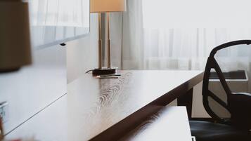 A modern room with a wooden desk, a black office chair, a lamp, and a window with blinds.