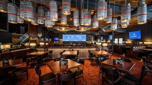 Zona bar ampia con diverse opzioni di posti a sedere e un grande schermo che mostra contenuti.