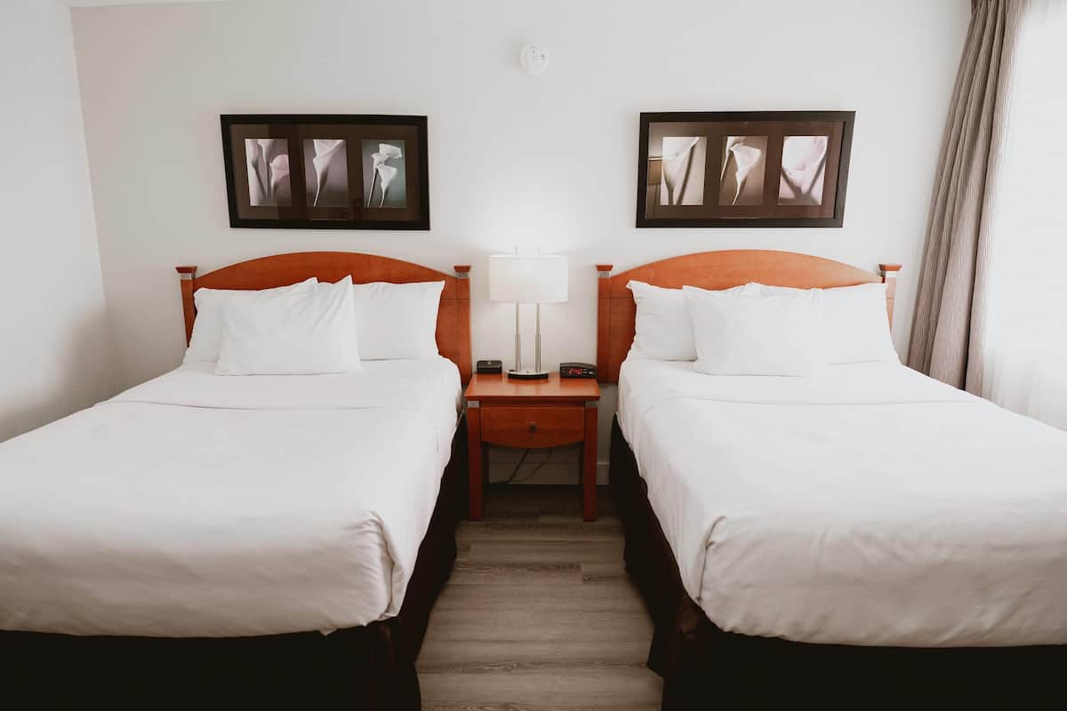 A hotel room with two single beds, a nightstand with a lamp, and framed artwork on the wall.