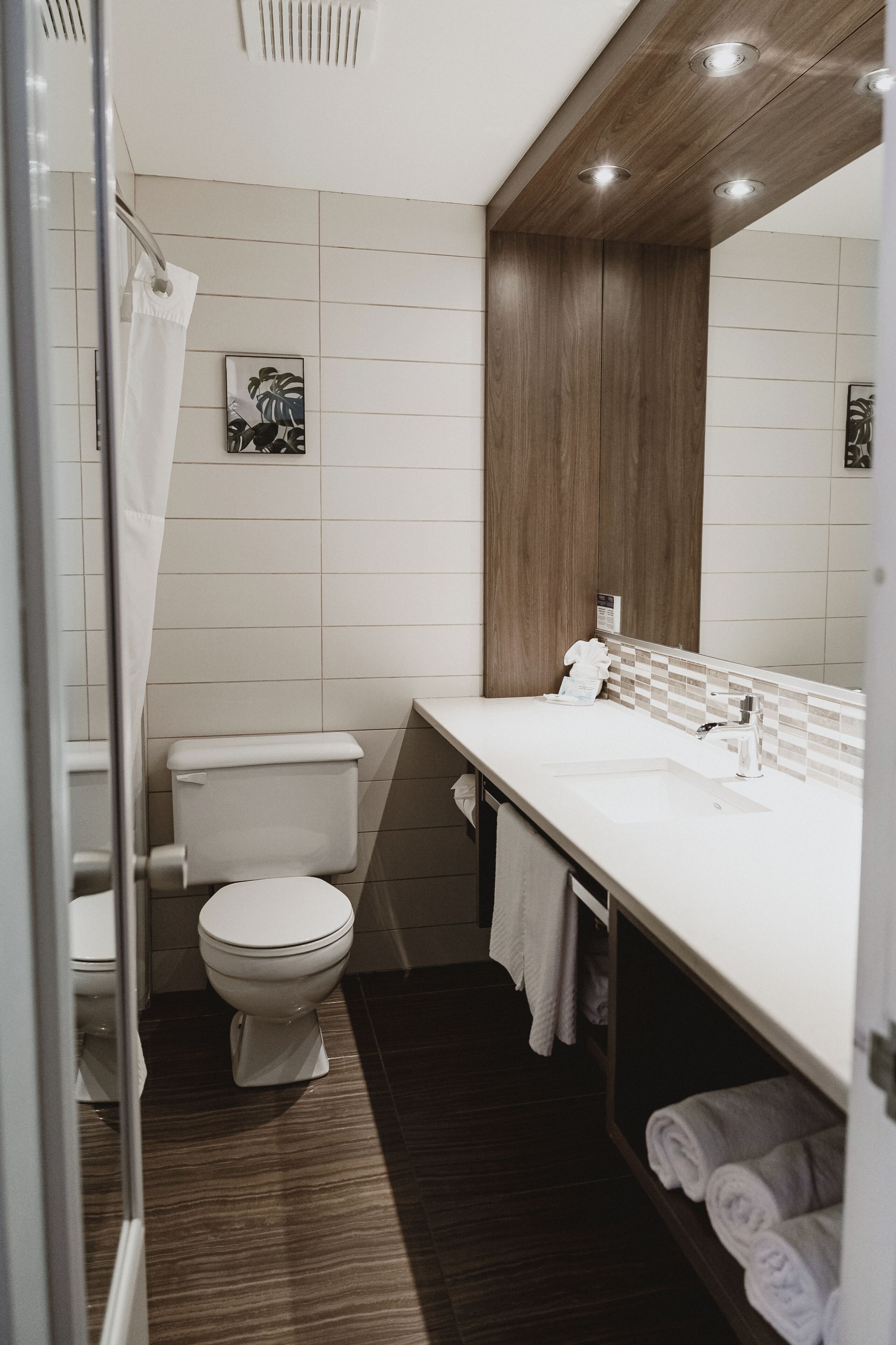 A modern bathroom with a white toilet, a wooden vanity, and a large mirror.