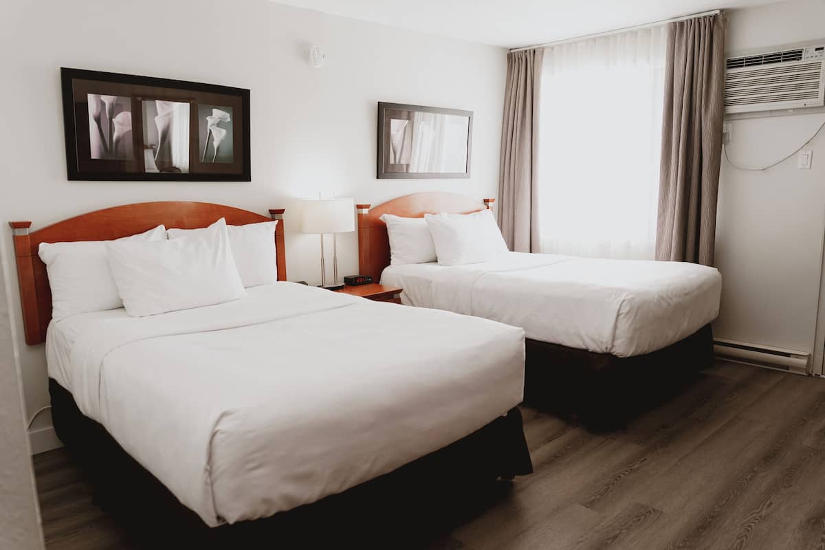 Una habitación de hotel con dos camas, una mesita de noche, una lámpara y un cuadro en la pared.