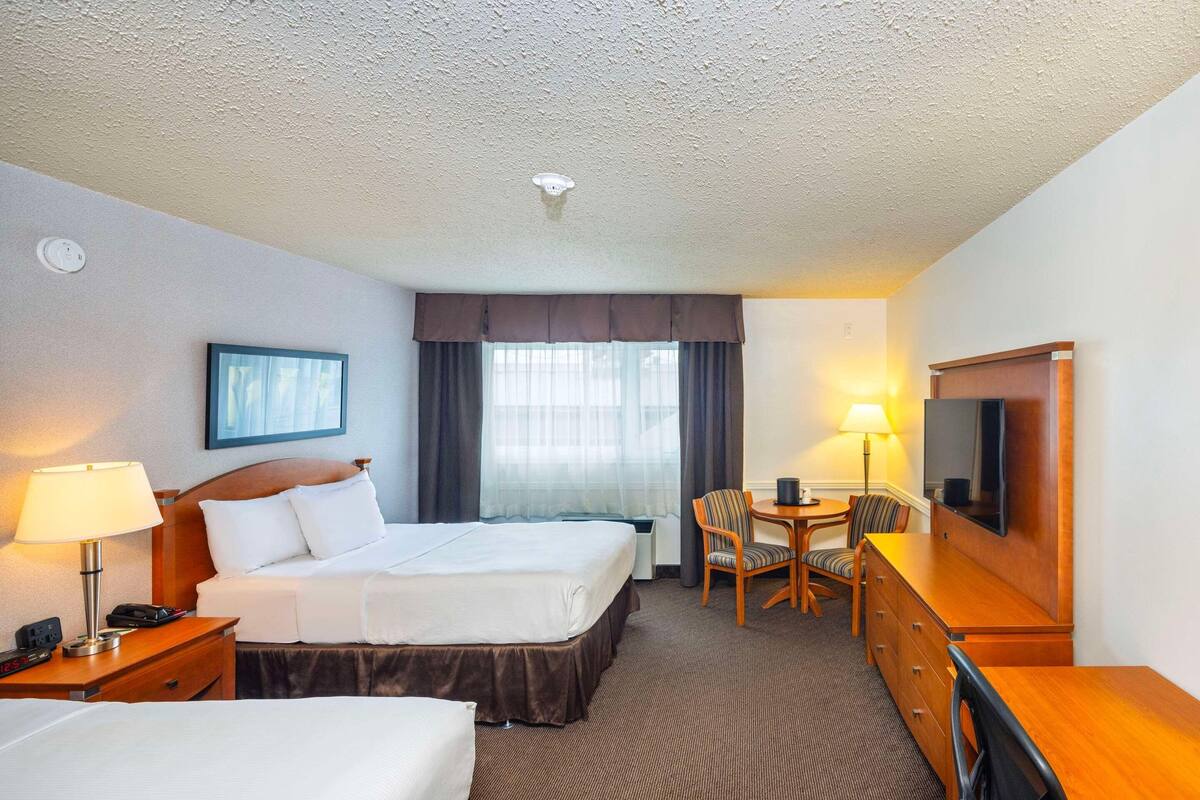 Una habitación de hotel con dos camas, un escritorio, una silla, un televisor y una lámpara.