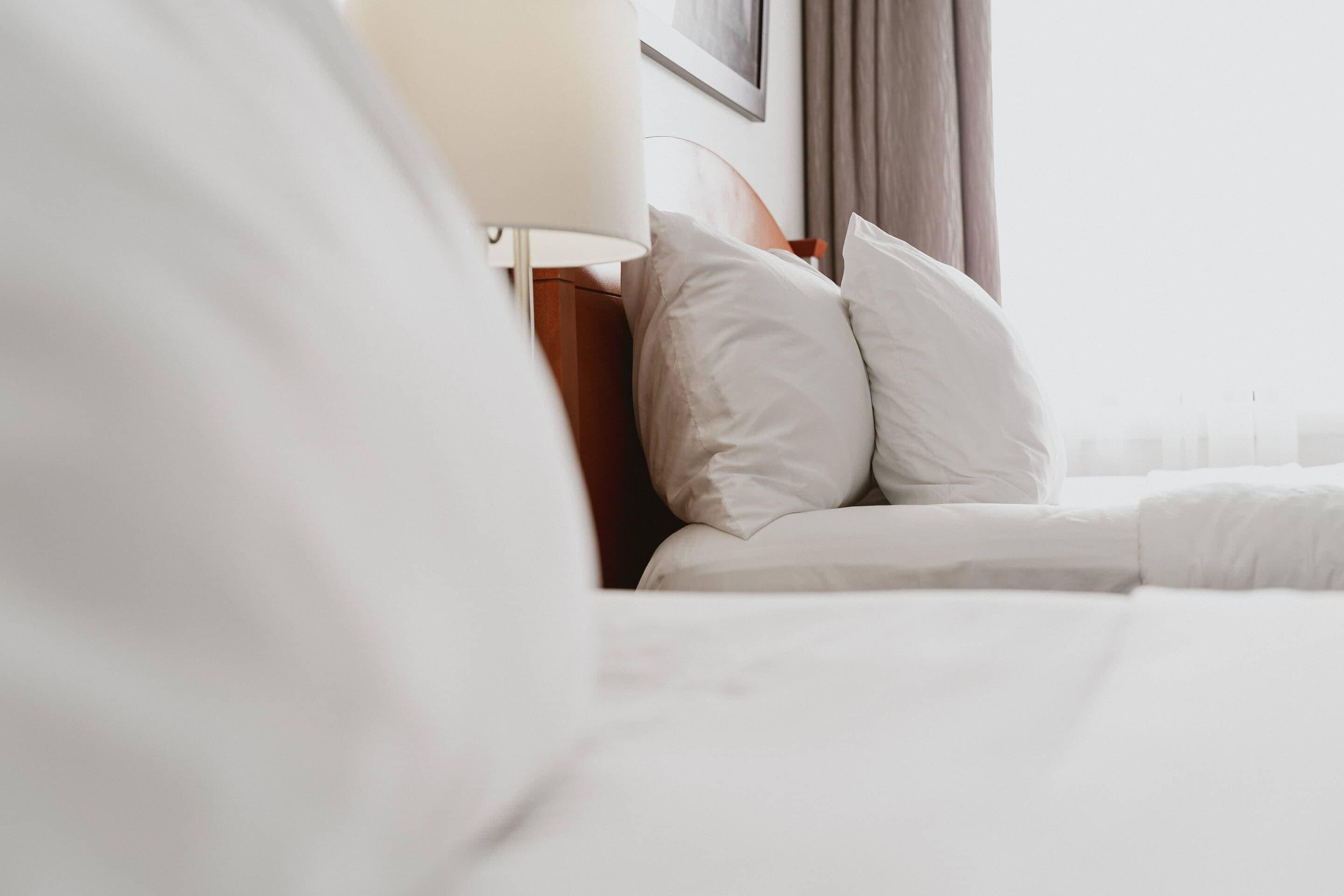 Uma cama bem arrumada com lençóis brancos, cabeceira de madeira e abajur.