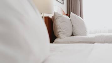Uma cama bem arrumada com lençóis brancos, cabeceira de madeira e abajur.