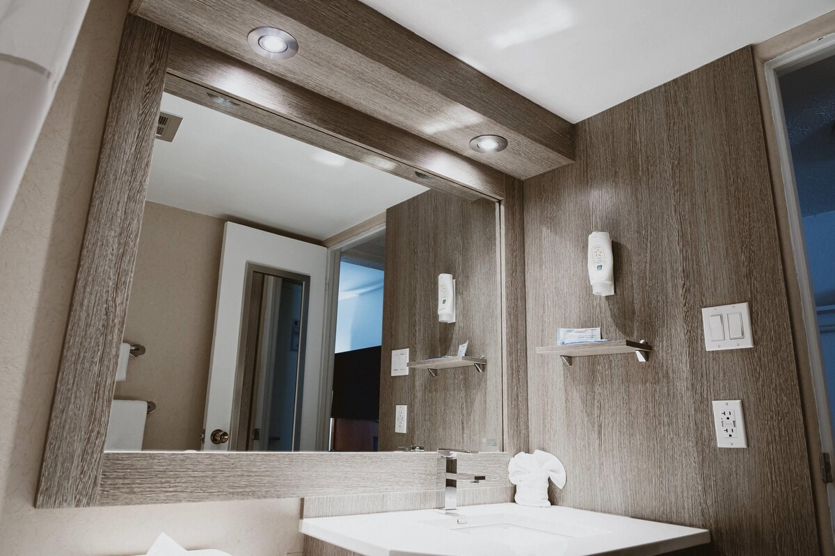 A modern bathroom with a large mirror, wooden paneling, a white sink, and a towel rack.