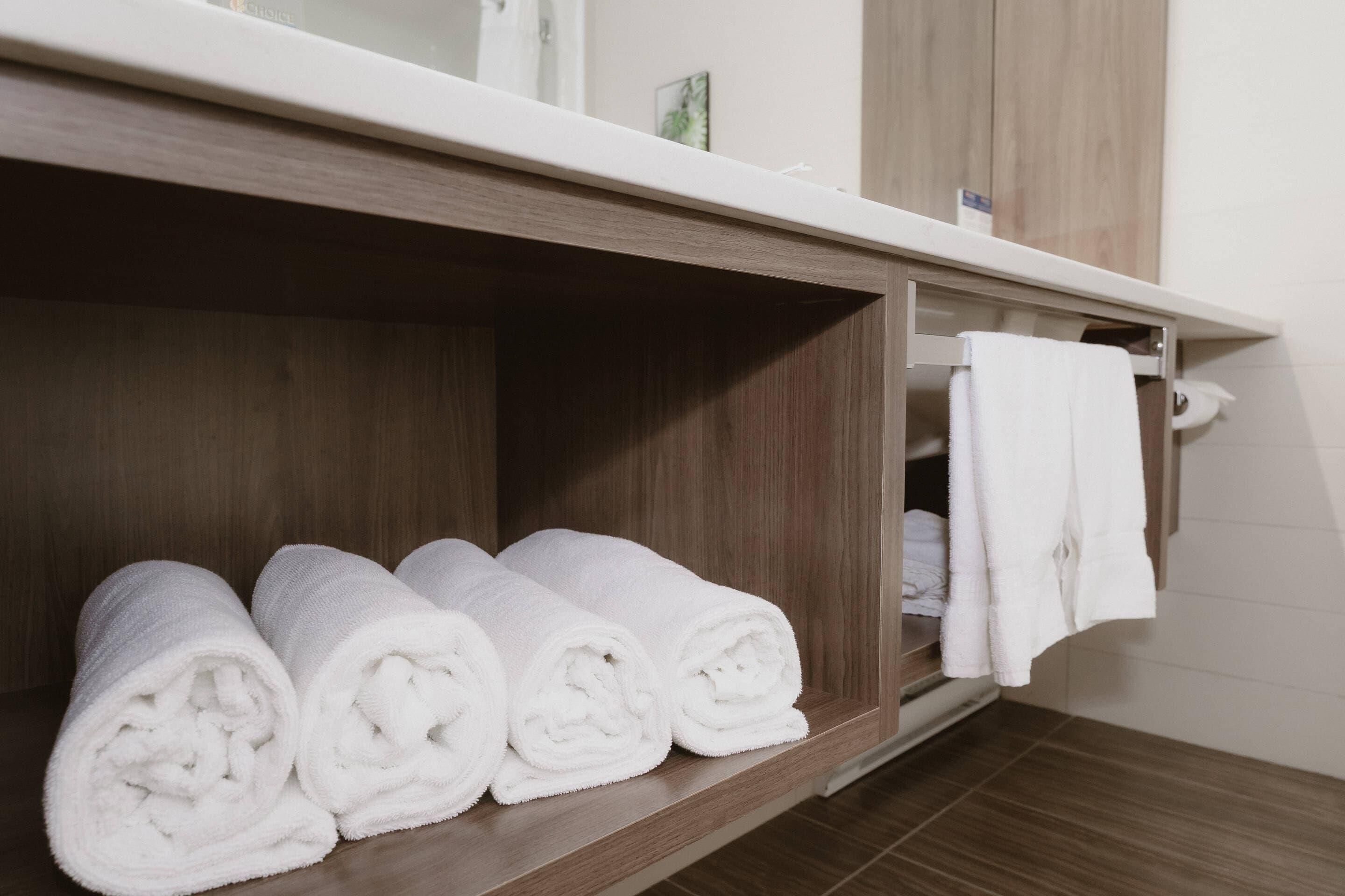 Une salle de bain avec des étagères en bois où sont rangées des serviettes blanches pliées.