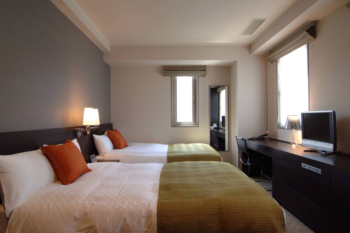Una habitación de hotel con dos camas, un escritorio con ordenador y televisión.