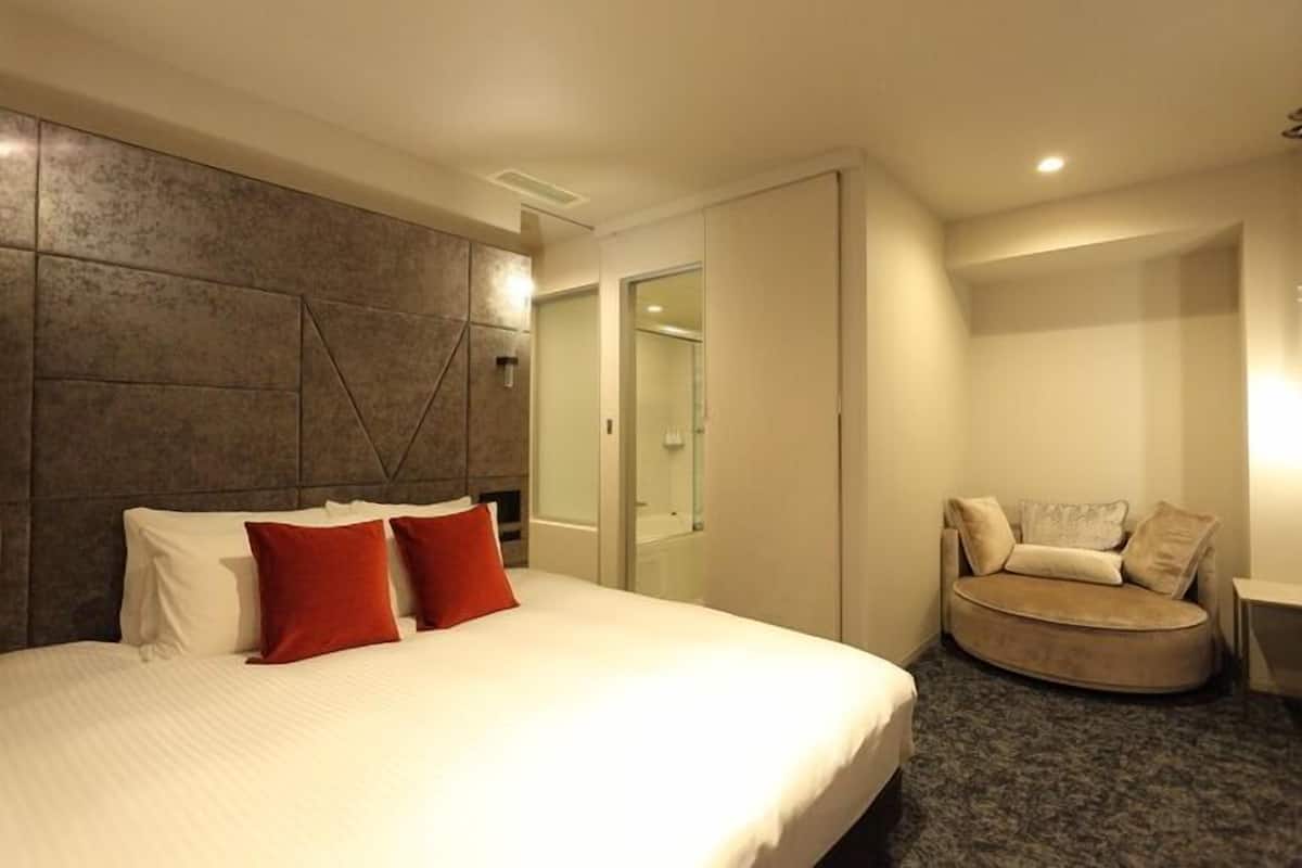 Habitación de hotel con una cama grande, un área de descanso circular, un vestidor y un baño con puerta de cristal.