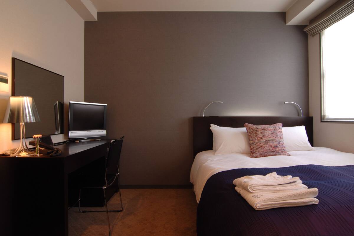 Una habitación de hotel con una cama, un escritorio con una computadora portátil, una silla y un televisor.