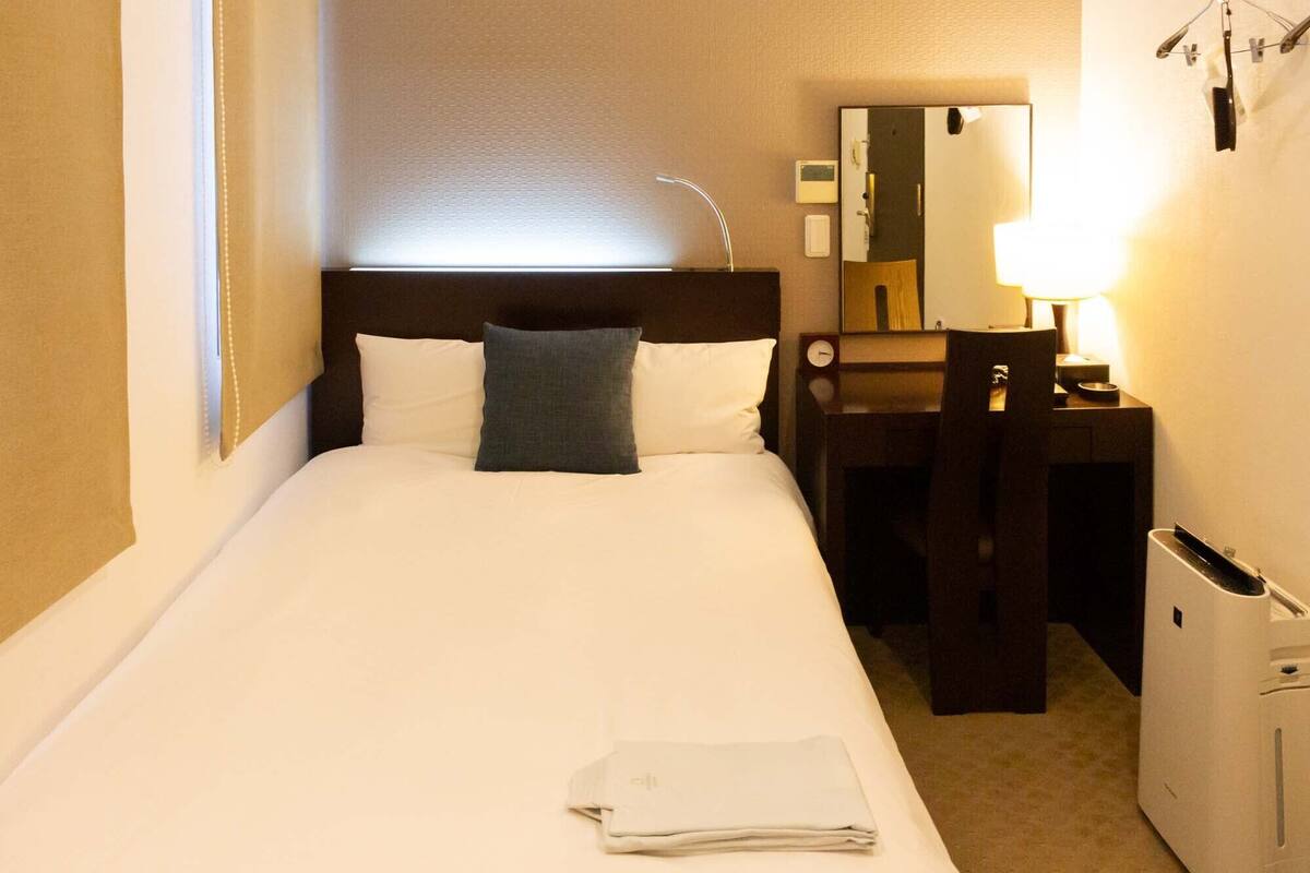 Une chambre d’hôtel comprenant un lit, une table de chevet avec une lampe, un miroir et un petit bureau avec une chaise.