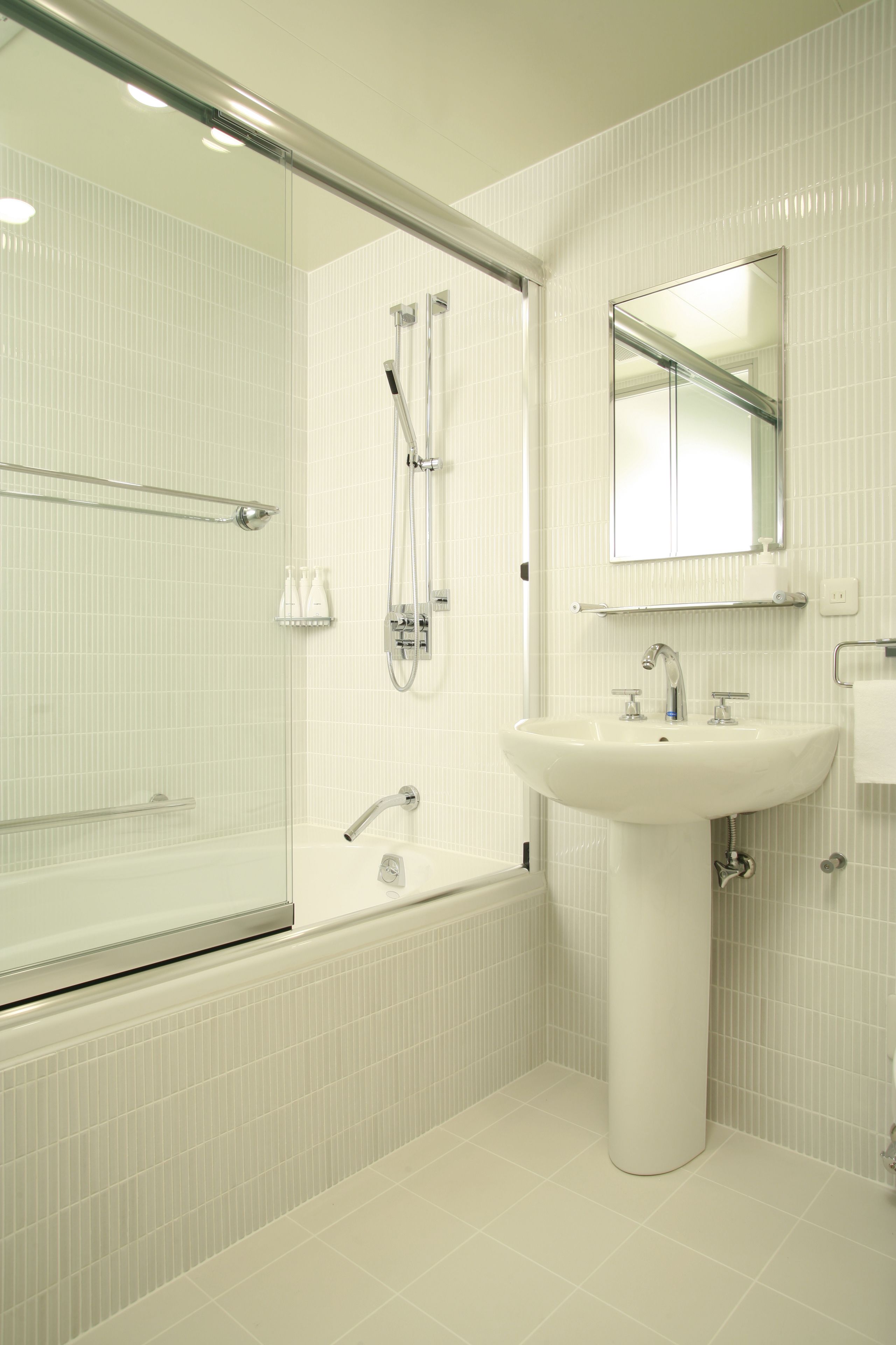 Une salle de bain moderne avec une douche à parois de verre, un lavabo sur colonne et un meuble-lavabo avec un grand miroir.