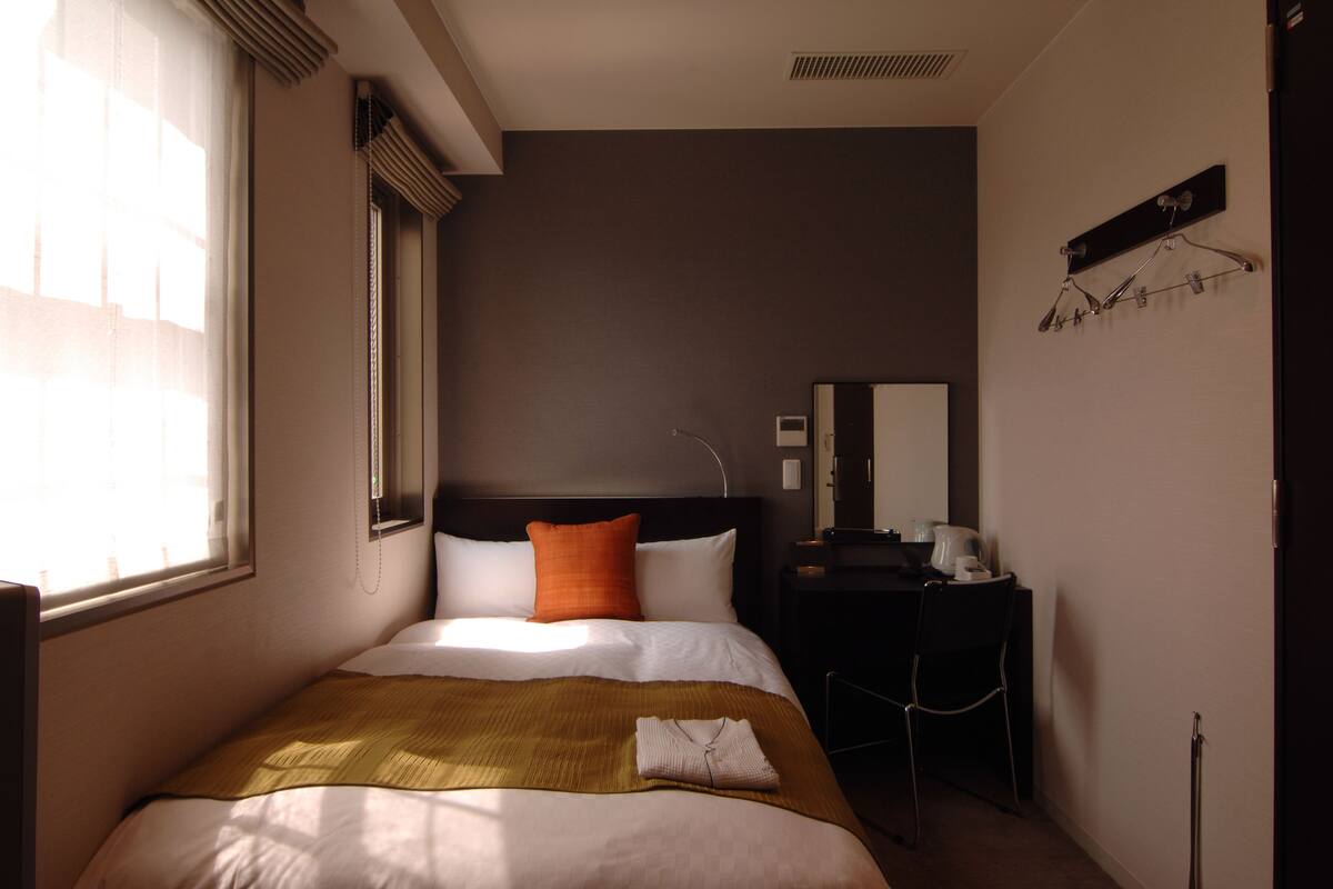Una habitación de hotel con una cama, un escritorio, una silla, un espejo y una ventana.