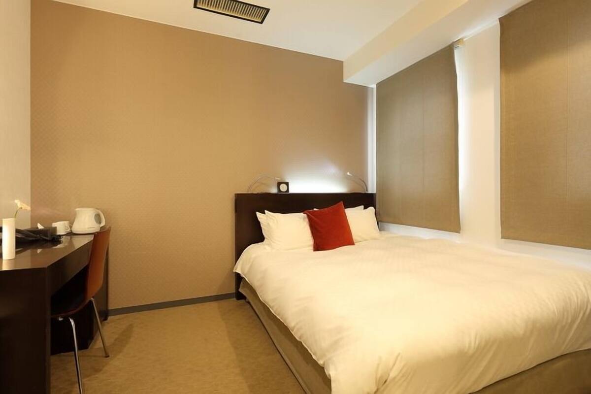 Una habitación de hotel con cama, escritorio, silla y ventana con cortinas.