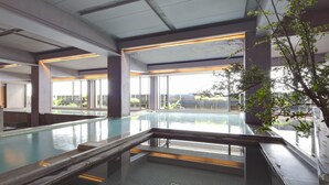 Ein moderner, überdachter Schwimmbereich mit Glaswänden, Fliesenboden und Blick ins Freie.