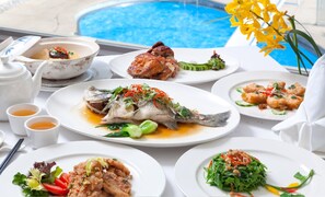 Une table dressée avec divers plats, notamment du poisson, des légumes et un dessert, avec une piscine en arrière-plan.