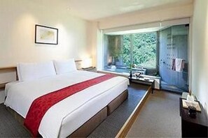 Une chambre d’hôtel avec un grand lit, un bureau et une fenêtre donnant sur un paysage verdoyant.