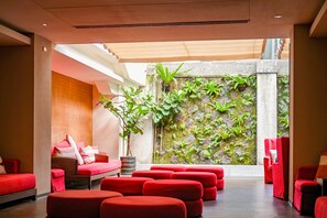 Un espace de détente moderne avec des sièges rouges, une grande plante en pot et une vue sur un mur végétal.