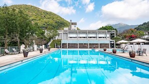 Ein modernes Hotel mit Schwimmbad, Sitzgelegenheiten im Freien und Blick auf einen Berg.