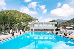 Un hotel moderno con piscina, mobiliario exterior y vistas a la montaña.