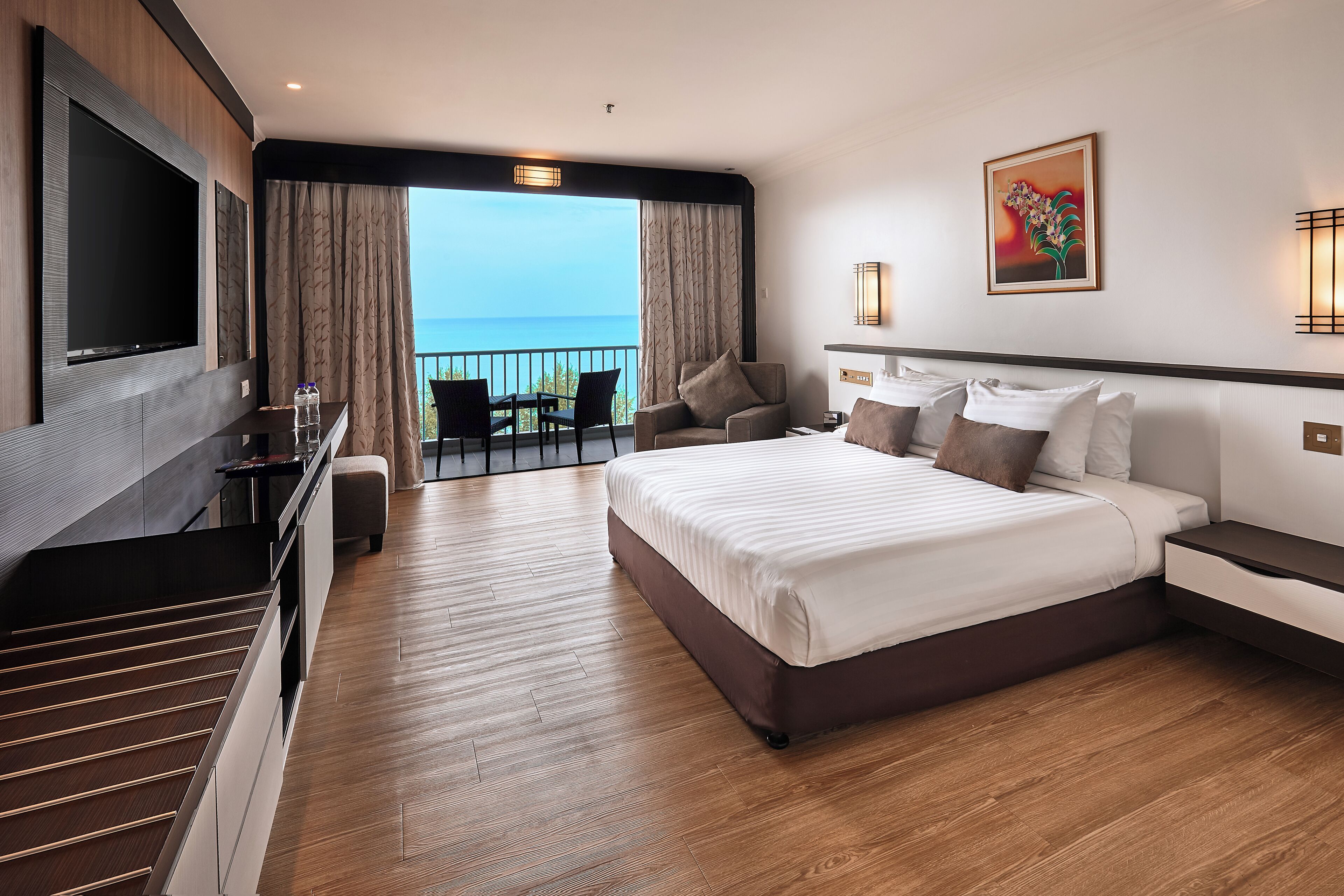 Une chambre d’hôtel moderne dotée d’un grand lit, d’une télévision, d’un balcon avec vue sur la mer et d’un coin repas.