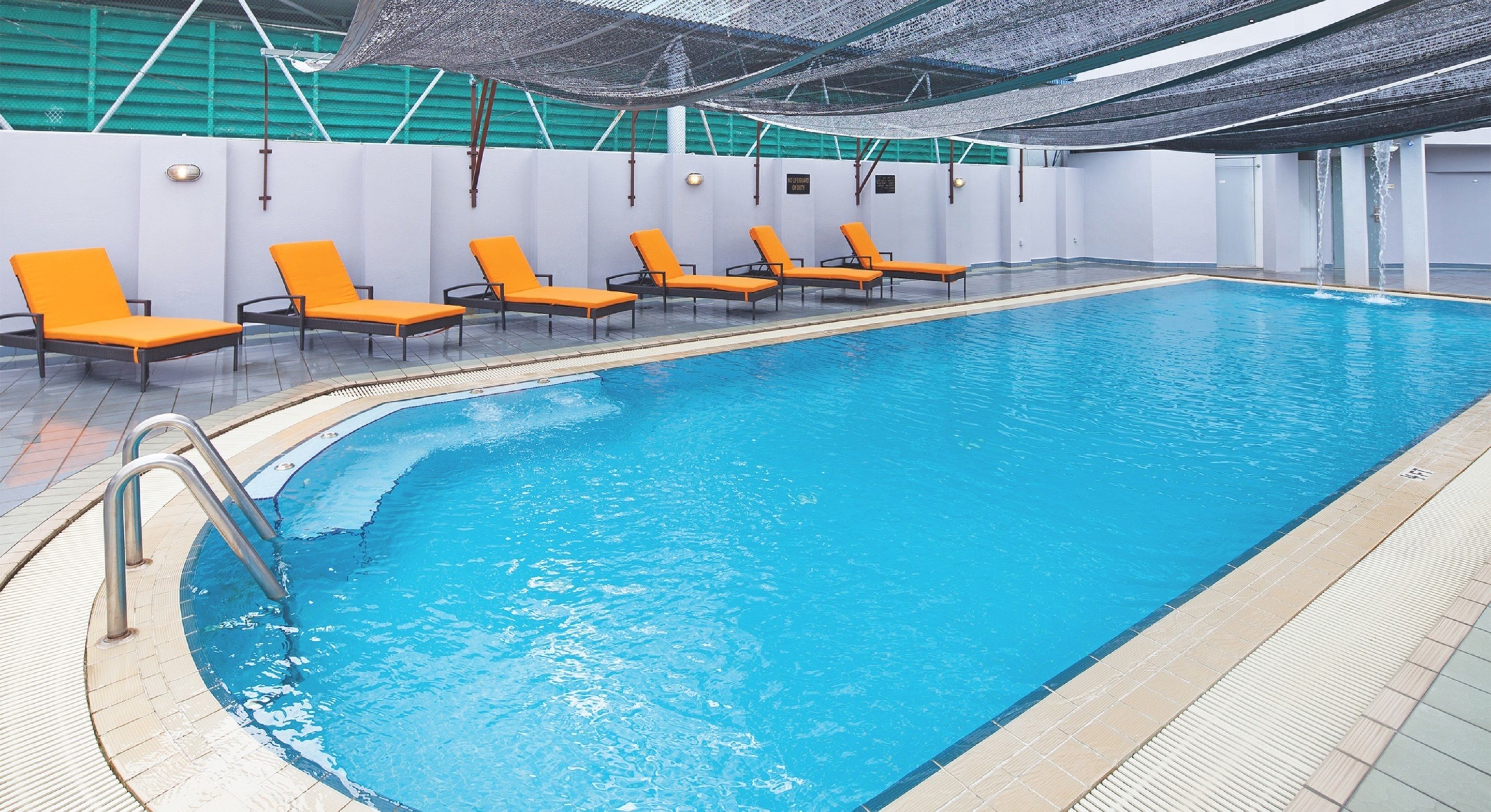 Une piscine entourée de chaises longues orange et d’une terrasse carrelée.