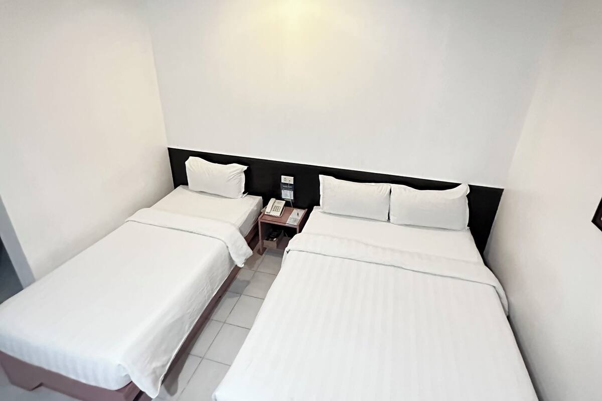 A hotel room with two single beds, a bedside table with a phone, and a wall-mounted light.