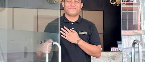 A man standing in front of a hotel reception with a glass door, a clock, and chandeliers on the wall.