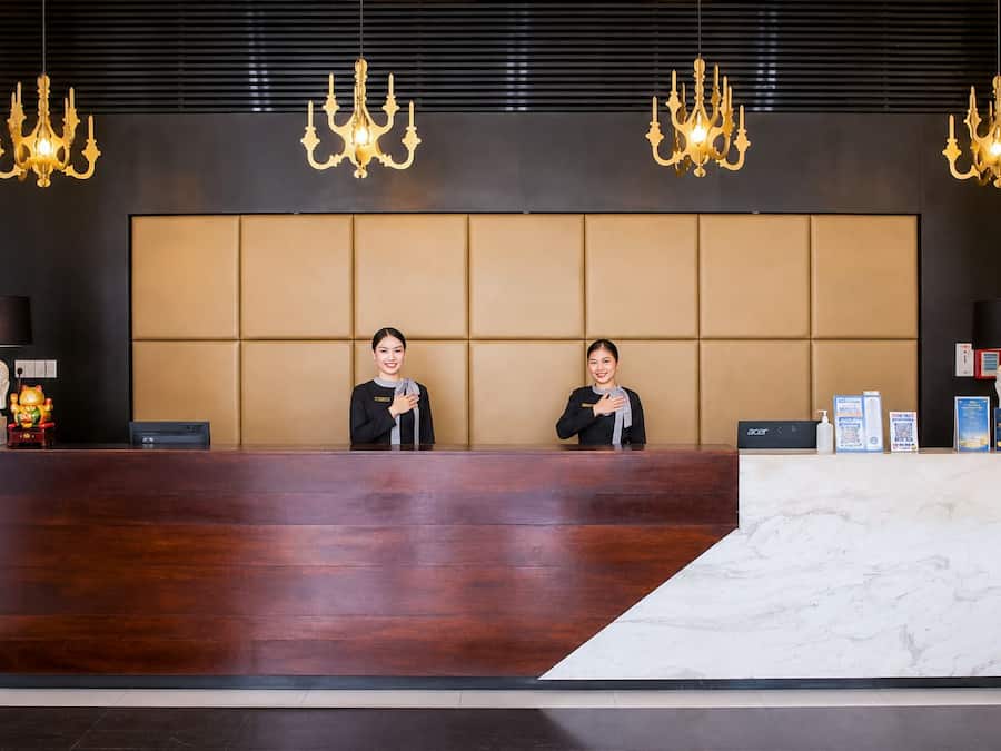 A reception desk with two staff members, a large padded headboard, and chandeliers.