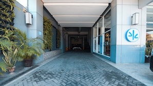 Ein gepflasterter Weg führt zu einem Gebäudeeingang mit blau-weißer Fassade, Blumentöpfen und einem Schild, das eine Parkverbotszone kennzeichnet.