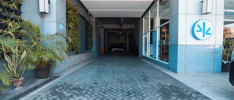 A paved walkway leading to a building entrance with a blue and white facade, potted plants, and a sign indicating a no parking zone.