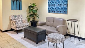 A living room with a sofa, armchair, ottoman, and a small table. There are two potted plants and two wall art pieces. - Hotel Pier Cuatro (Cebu City)