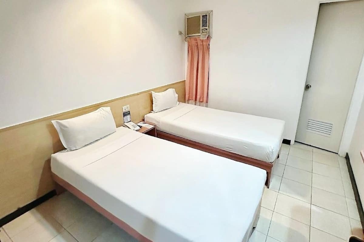 A hotel room with two single beds, a small bedside table with a phone, a wall-mounted air conditioning unit, and a door with a vent.