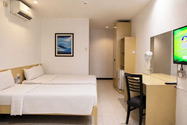 Habitación de hotel con dos camas, un escritorio con silla, televisor y aire acondicionado instalado en la pared.