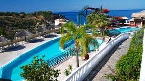 Piscina de resort con tobogán de agua, palmeras y vista al océano.