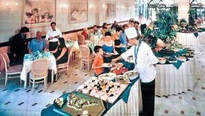 Un salón de comedor formal con varias mesas, meseros y comensales.